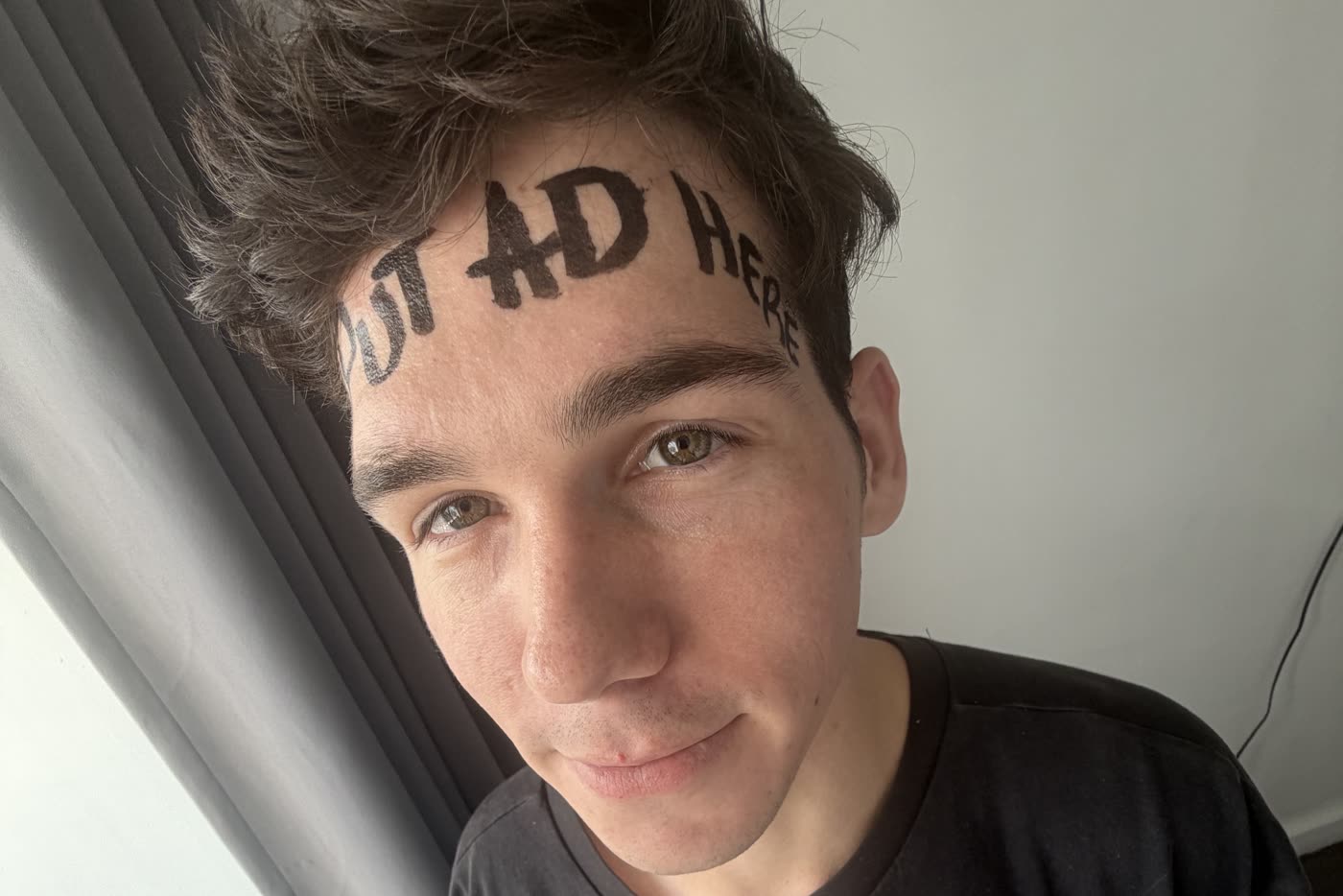 Landon Little photographed with PUT AD HERE written across his forehead in black marker. The forehead is unit F-01, the single advertising placement currently for sale.